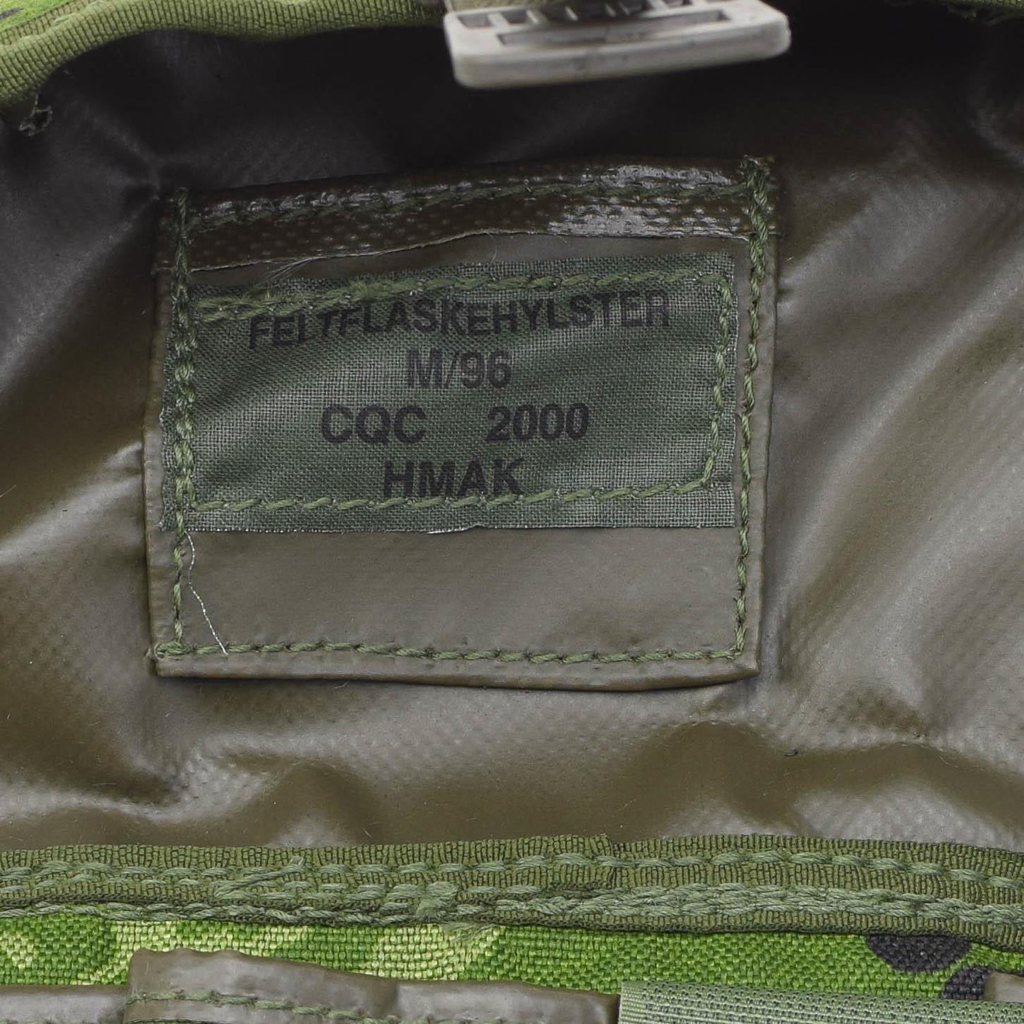 Danijos kariuomenes universalus deklas M96 marginimas etiketė su gamybos informacija žalios spalvos audinyje