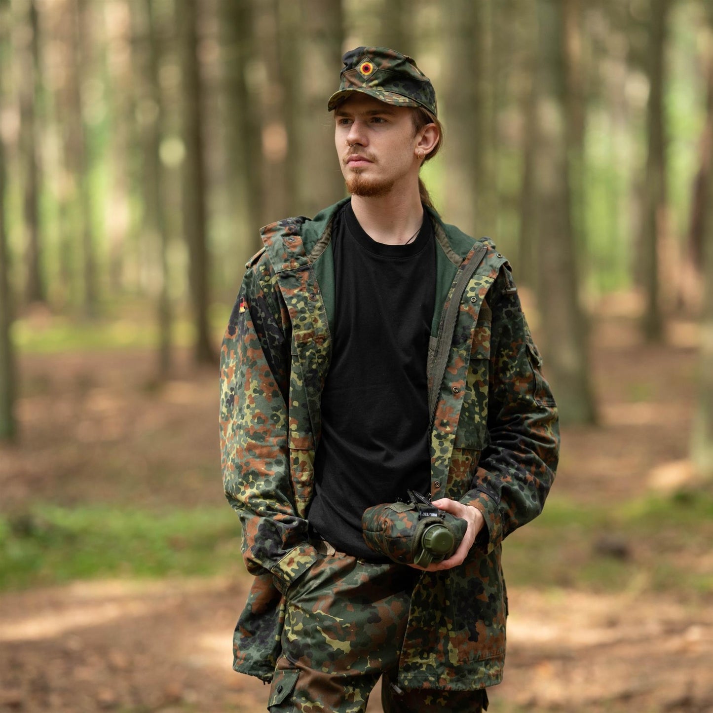 JAV kariuomenės vandens gertuvė su dangteliu nešiojama vyro miško aplinkoje kariškoje aprangoje.