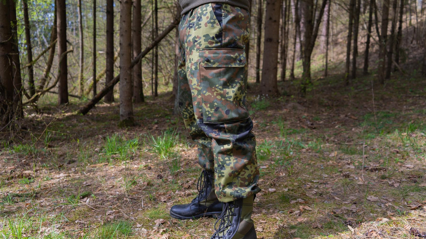 Vokiečių kariuomenės lauko uniformos kelnės Flecktarn marginimo miško aplinkoje dėvimos ant aukšto žmogaus.