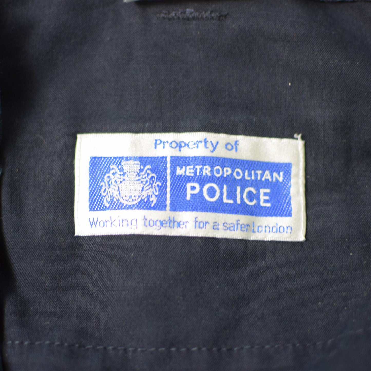 Britanijos policijos kelniu etiketė su Metropolitan Police logotipu ant mėlyno uniforminio audinio