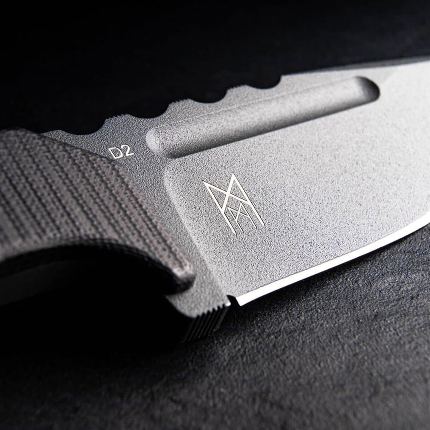 Boker Plus Little Dvalin Black peilis is D2 plieno, detali nuotrauka rodo ašmenu struktura ir logotipa ant pilko geleztes pavirsiaus