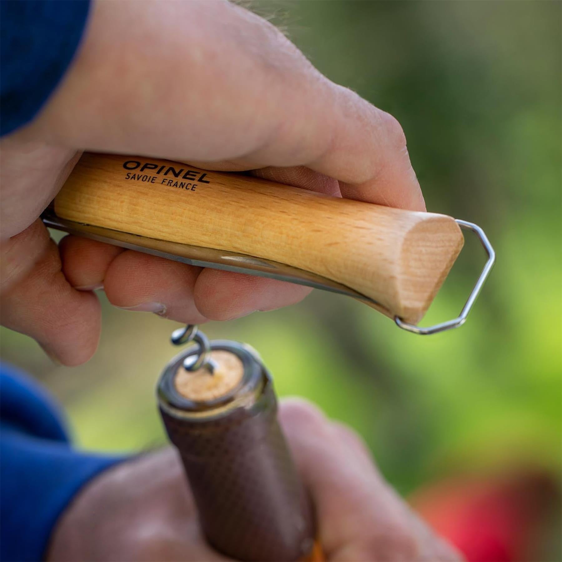 Opinel N°10 daugiafunkcinis kišeninis peilis su kamščiatraukiu atidarinėja vyno butelį gamtoje.